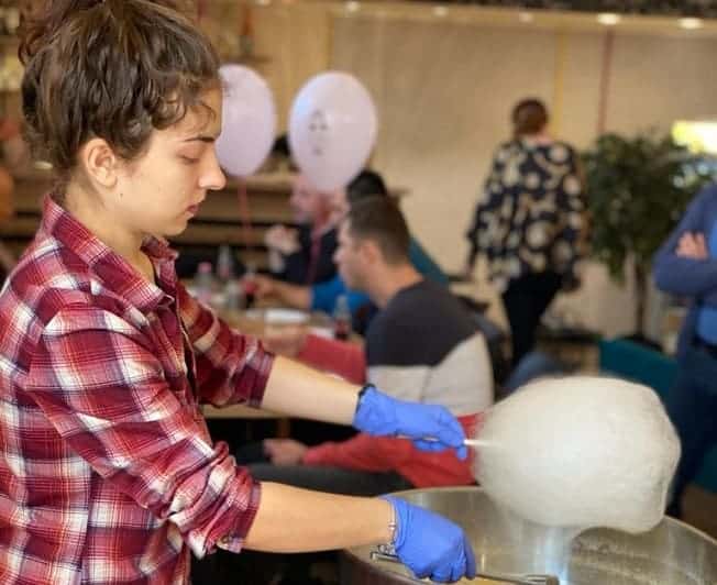 Persoană cu mănuși prepară o porție albă de vată de zahăr deasupra cuvei aparatului.